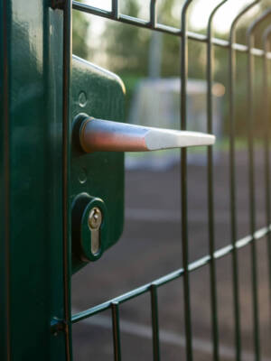 Handle with a lock on the open gate of a sports ground fenced with a welded mesh fence, outdoors, in the evening at sunset. Close-up.