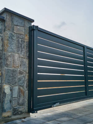 Wide automatic sliding gate with remote control installed in high stone fense wall. Security and protection concept Wide automatic sliding gate with remote control installed in high stone fense wall. Security and protection concept.